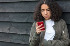 a woman with curly hair looking at her cell phone while leaning against a black wall