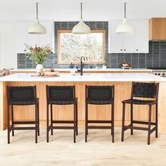 a kitchen with four stools in front of an island and counter top, along with three lights hanging from the ceiling