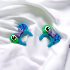 two blue and green hair clips sitting on top of a white cloth covered bed sheet