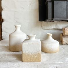 three white vases sitting on top of a table next to each other in front of a fireplace