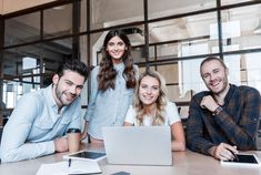 three people sitting at a table in front of a laptop computer with their arms around each other