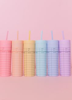 five pastel colored cups with straws lined up in a row on a pink background