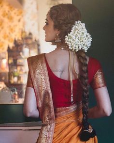 a woman with braids and flowers in her hair wearing an orange sari, looking out the window