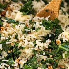 rice and greens are mixed together in a bowl with a wooden spoon on the side