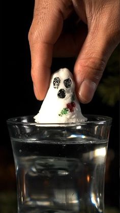 a hand is dipping something into a glass filled with water and white stuff in the shape of a skull