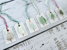 christmas ornaments are hanging from string on white wooden planks with green and red twine