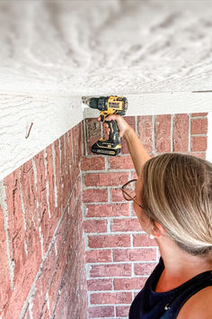 a woman is using a driller to fix a brick wall with a power drill