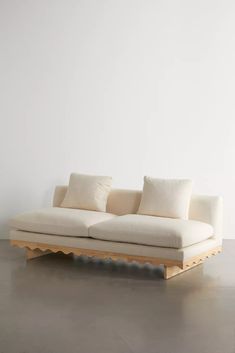 a white couch sitting on top of a wooden floor next to a wall with two pillows