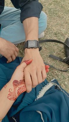 two people with henna tattoos on their hands holding each other's hand while sitting in the grass