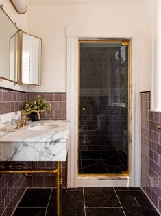 a bathroom with marble counter tops and gold trim around the shower door, along with black tile flooring