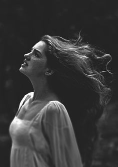 black and white photo of woman with long hair looking up at the sky in front of trees