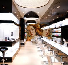 the interior of a hair salon with long tables and chairs in front of an artistic mural on the wall