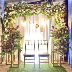 two chairs sitting under a floral covered stage set up for a wedding or reception ceremony