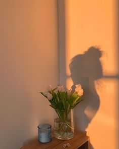 a vase filled with flowers sitting on top of a wooden table next to a wall