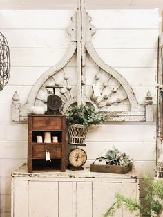 an old dresser with some plants and other things on it in front of a white painted wall