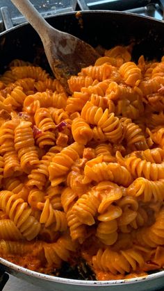 a large pot filled with pasta and meat on top of a gas burner next to a wooden spoon