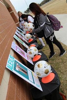 several girls are lined up with soccer balls on the side of a building and one girl is holding a backpack