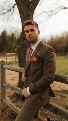 a man in a suit leaning against a fence with his hands on his hips and looking at the camera