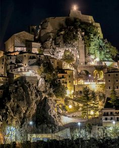 a night time view of a village on top of a hill with trees and lights