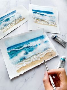 someone is painting some watercolors on the beach with blue and white waves in the ocean