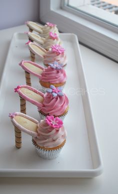 cupcakes with pink frosting and bows are lined up on a white tray