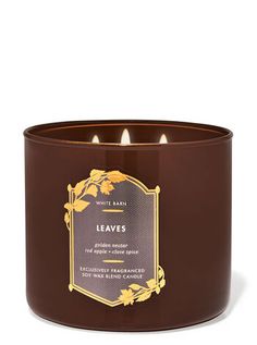 a candle that is brown and has leaves on the front, with a gold trim around it