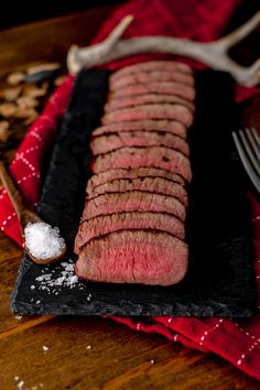 a piece of steak sitting on top of a black plate next to a fork and spoon