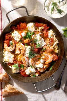 a skillet filled with shrimp, tomatoes and feta cheese on top of a table