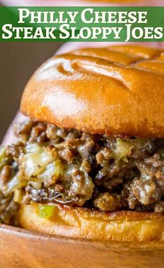 a close up of a hamburger on a wooden plate with text that reads phily cheese steak sloppy joes