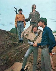 four men are standing on top of a pile of wood and one man is holding a large piece of cardboard