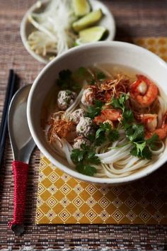 a bowl of shrimp and noodle soup with chopsticks next to it on a place mat