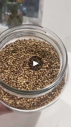 a person holding a glass jar filled with brown seeds and looking into the camera lens