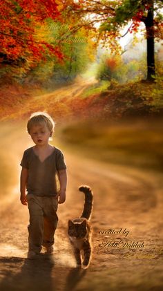 a little boy walking down a dirt road with a cat on it's back