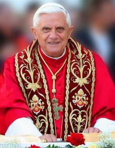 an older man wearing a red and gold priest's outfit with chains around his neck