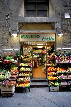 an open market with many fruits and vegetables on display in front of the store's entrance