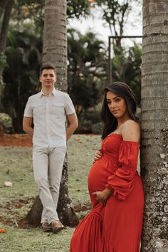 a pregnant woman leaning against a palm tree