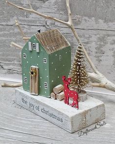 a small green house with a red deer figurine next to it on a wooden table