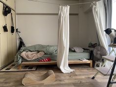 a cat sitting on top of a bed in a room with wooden floors and white curtains