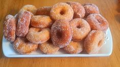 a pile of sugared donuts on a white plate sitting on a wooden table