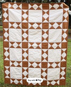 a brown and white quilt on grass with trees in the background