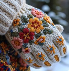 a pair of white knitted gloves with colorful flowers on the outside and inside of them