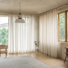 a living room filled with furniture and large windows covered in white drapes, along with a rug on top of a hard wood floor