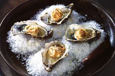 four oysters are sitting on top of some sea salt in a black bowl with a wooden spoon