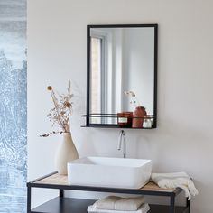 a white sink sitting under a mirror next to a shelf with towels and vases