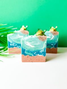 two small square cakes with strawberries on top sitting on a white table next to a green plant