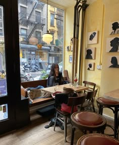 a woman sitting at a table in front of a window with pictures on the wall