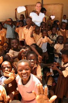 a woman standing in front of a group of children with their hands up and smiling