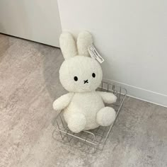 a white stuffed rabbit sitting on top of a metal wire basket next to a wall