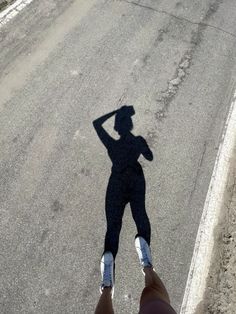 a person standing in the middle of an empty road with their shadow on the ground