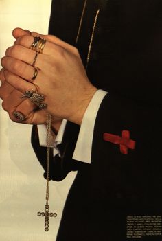 a man in a tuxedo holding two rings and a cross on his finger